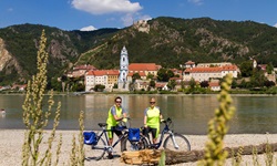 Zwei Radler posieren vor dem Stift Dürnstein für ein Foto.