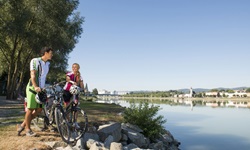 Ein Radlerpärchen macht am Donauufer Pause und genießt den Ausblick auf Aschach.