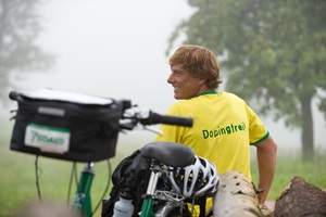 Ein Radfahrer macht eine Pause an einem Holzstapel und hat ein gelbes T-Shirt mit der Aufschrift "Dopingfrei" an