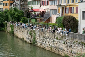 Menschen sitzen auf der Mauer mit ihren Beinen in Richtung Neckar an der Promenade in Tübingen