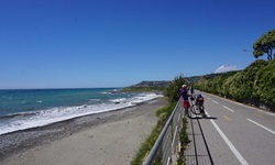 Eine Radfahrerin in Ligurien macht am Rand eines Radwegs, der direkt an der Küste entlangführt, Pause.