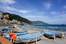 Mit blau-weißen Planen abgedeckte Ruderboote liegen bei Alassio am Strand.