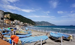 Mit blau-weißen Planen abgedeckte Ruderboote liegen bei Alassio am Strand.
