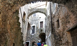 Touristen bummeln durch einen ligurischen Ort, dessen Häuser teilweise durch kleine Brücken miteinander verbunden sind.
