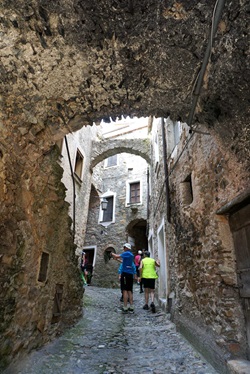 Touristen bummeln durch einen ligurischen Ort, dessen Häuser teilweise durch kleine Brücken miteinander verbunden sind.