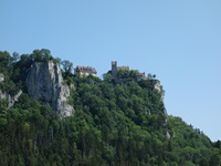 Blick auf eine auf einem Steinmassiv ragende Burg vom Donautal