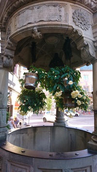 Ein Brunnen mit Säulen und Dach, der mit Blumenampeln geschmückt ist
