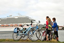 Eine Familie mit Rädern steht am Ufer und blickt auf ein Kreuzfahrtschiff