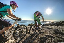 Zwei Mountainbiker - ein Mann und eine Frau - biken auf einem steinigen Trail in Süddalmatien am Meer entlang auf die gleißende Sonne zu.