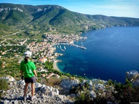 Eine Radlerin mit weißem Helm, grünem T-Shirt und schwarzer Radlerhose blickt von einer Klippe in Süddalmatien auf das unter ihr liegende Meer.