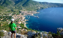 Eine Radlerin mit weißem Helm, grünem T-Shirt und schwarzer Radlerhose blickt von einer Klippe in Süddalmatien auf das unter ihr liegende Meer.