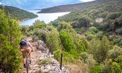 Ein Mountainbiker bikt einen steinigen Weg hinab. Im Hintergrund ist das Meer zu sehen