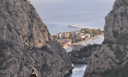 Ein Mountainbiker steht auf einem Aussichtsfelsen mit Statue in Omis und blickt auf den Canyon und die Mündung der Cetina in das Adriatische Meer in Süddalmatien