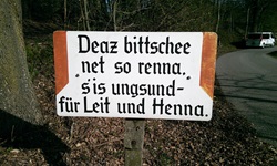 Ein Schild am Wegesrand mit der Aufschrift: "Dear bittschee net so renna. s´is ungsund - für Leit und Henna"