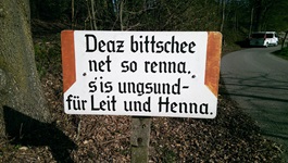 Ein Schild am Wegesrand mit der Aufschrift: "Dear bittschee net so renna. s´is ungsund - für Leit und Henna"
