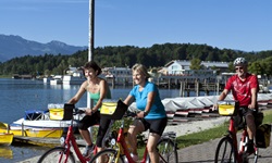 Drei Fahrradfahrer fahren an einer Bootsanlegestelle am Chiemsee vorbei