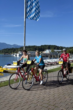 Drei Fahrradfahrer fahren an einer Bootsanlegestelle am Chiemsee vorbei