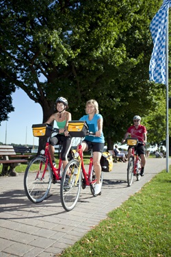 Radler fahren auf einem gepflasterten Weg mit Sitzbänken am Chiemsee entlang