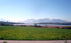 Blick über Wiesen, Felder, einen See und die traumhafte Alpenkulisse in Bayern