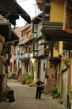 Ein Mann steht in einer Gasse von typischen Fachwerkhäusern in Eguisheim im Elsass