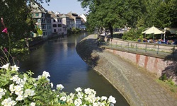 Häuser an einem Kanal im Elsass von einer mit Blumen geschmückten Brücke aus gesehen.