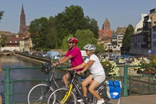 Ein Radlerpärchen auf einer Brücke in Straßburg; im Hintergrund ist das Straßburger Münster zu erkennen.