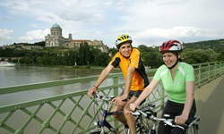 Zwei Radler fahren über eine Brücke in Esztergom, im Hintergrund die Basilika