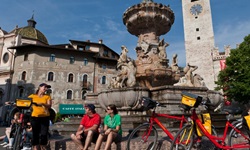Drei Radler machen beim Neptunbrunnen auf dem Domplatz von Trient Pause.