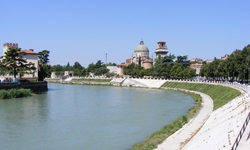 Eine Radfahrerin hat es sich am Ufer der Etsch in Verona gemütlich gemacht. Nicht weit entfernt erhebt sich die Kuppel der Kirche San Giorgio in Braida.