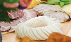 Eine schmackhafte Brotzeit mit Rettich, verschiedenen Schinkenspezialitäten und Gemüse auf einem mit Blumen geschmückten Tisch.