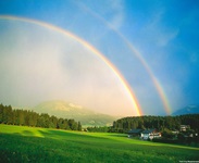 Ein wunderschöner doppelter Regenbogen über einem am Alpe-Adria-Radweg gelegenen, von grünen Wiesen und Wäldern umrahmten Dorf im Salzburger Land.