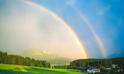 Ein wunderschöner doppelter Regenbogen über einem am Alpe-Adria-Radweg gelegenen, von grünen Wiesen und Wäldern umrahmten Dorf im Salzburger Land.