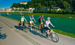 Vier Radler fahren auf einem asphaltierten Radweg an der Salzach entlang.