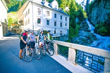 Vier Radler stehen in Bad Gastein auf einer Brücke und bewundern den mitten im Dorf gelegenen Wasserfall.