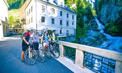 Vier Radler stehen in Bad Gastein auf einer Brücke und bewundern den mitten im Dorf gelegenen Wasserfall.