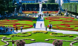 Sattgrüner Rasen, bunte Blumen und weiße Wege im Salzburger Mirabellgarten. Im Hintergrund sind der Dom und die Festung Hohensalzburg zu erkennen.