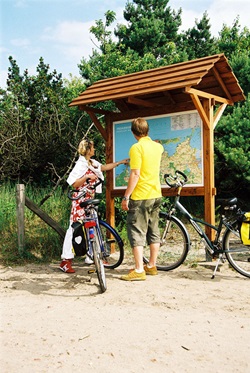 Zwei Fahrradfahrer stehen neben einer Infotafel, die sie betrachten