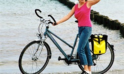 Eine Frau steht am Strand der Ostsee und hält ihr Rad fest