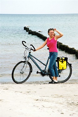 Eine Frau steht am Strand der Ostsee und hält ihr Rad fest