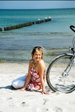 Eine Radlerin sitzt am Strand neben ihrem Rad