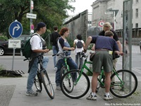 Eine Gruppe Radler steht an einer Kreuzung und blickt auf eine Infotafel, die über die Berliner Mauer berichtet