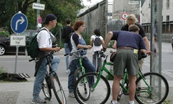 Eine Gruppe Radler steht an einer Kreuzung und blickt auf eine Infotafel, die über die Berliner Mauer berichtet