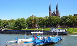 Eine weiß-blaue Fähre liegt am Flussufer der Maas und wartet auf die letzten Passagiere.