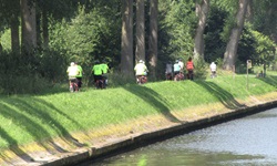 Eine Radlergruppe fährt an einem Wasserlauf entlang.