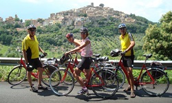 Vier Radfahrer machen eine Pause am Straßenrand und posieren vor einer Stadt, die hinter ihnen auf einem Hügel liegt