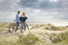 Zwei Radfahrer stehen auf einer Düne auf der Insel Föhr und blick auf das Meer