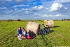 Zwei Fahrradfahrer machen an einem Strohballen auf einem Feld ein Picknick auf der Insel Föhr