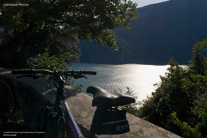 Ein Fahrrad lehnt an einer Mauer auf der Via Claudia Augusta, dahinter ist der Gardasee zu sehen