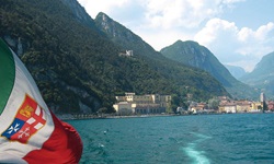 Blick vom Heck eines Ausflugschiffes über den Gardasee zu einer dort liegenden Stadt
