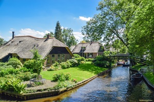Reetgedeckte Häuser und Blick zu einer Kanalbrücke in der größtenteils autofreien Ortschaft Giethoorn in den Niederlanden